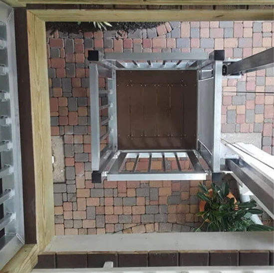 Shuttle Bolt-Together Cargo Lift Overhead view of a metal framed shaft for home elevators, surrounded by multicolored stone tiles and plants at the base.