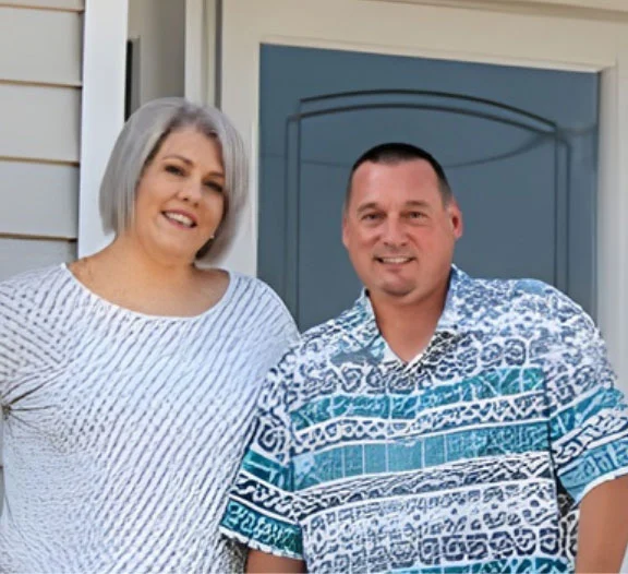 Smiling couple standing together outside a home entrance, next to a door.