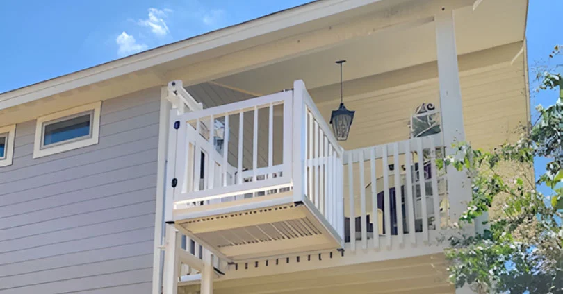 White home elevator with railing connects two levels of a house, enhancing accessibility under a blue sky.