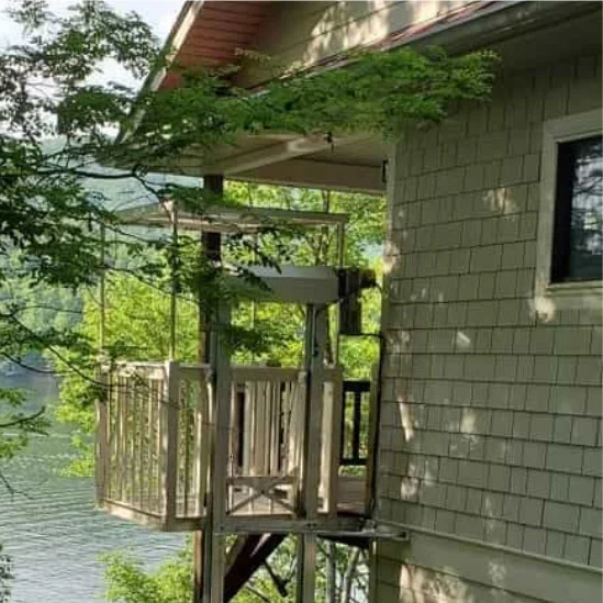 voyager + lift Home elevator attached to a lakeside house, surrounded by greenery, provides access to different levels of the building.